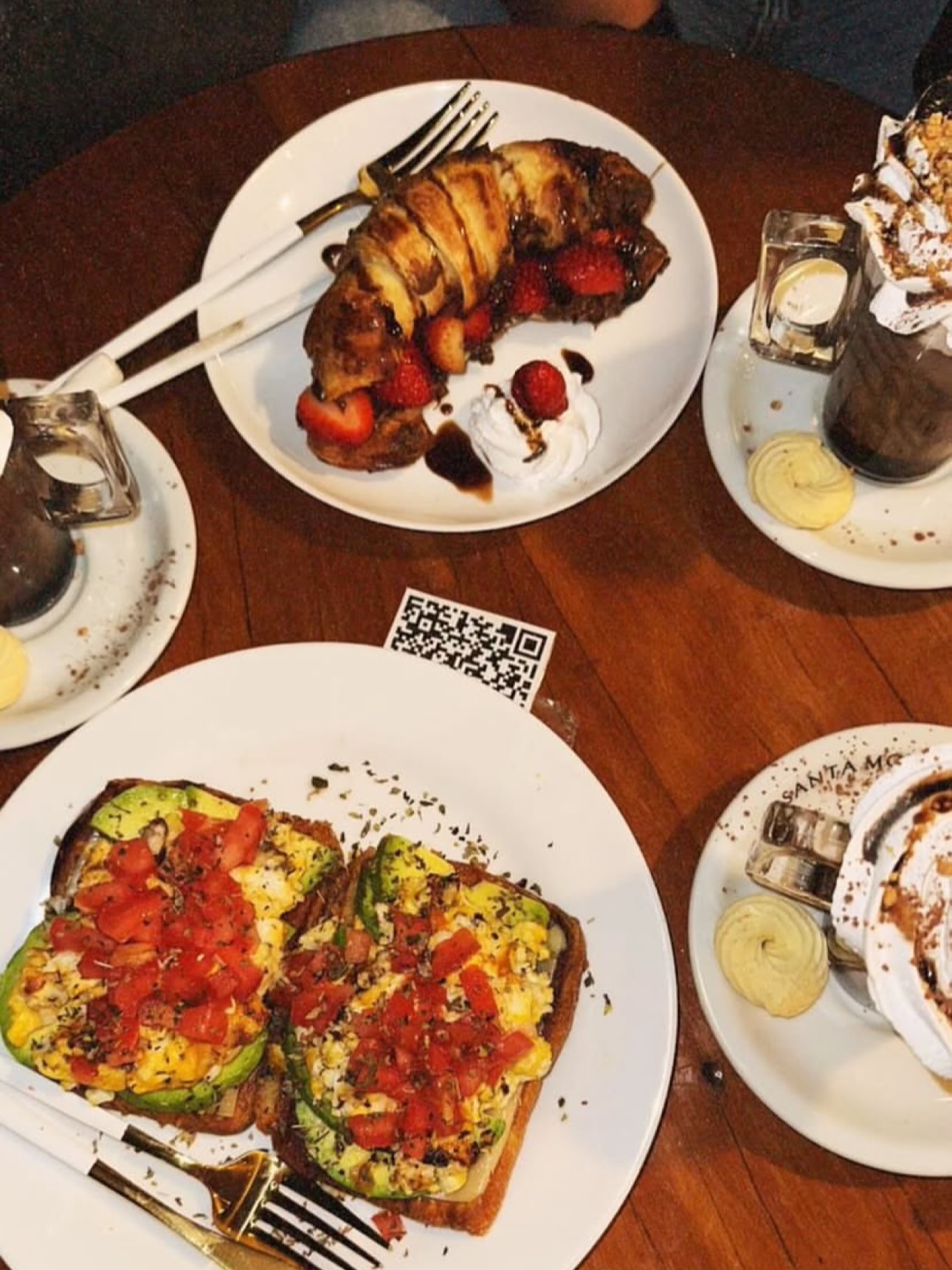 Avocado toast com ovos mexidos e tomate ao lado de um croissant com morangos